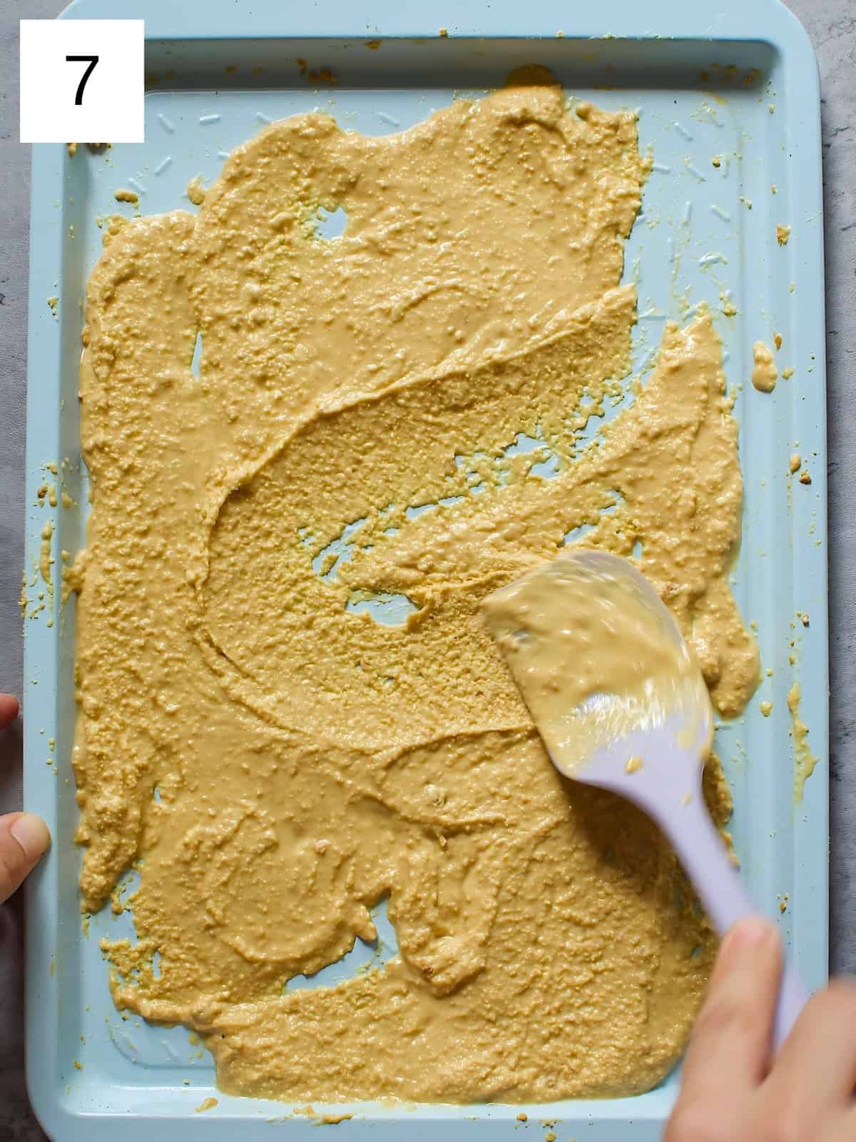 Melted white chocolate being on a baking tray being stirred with a baking spatula.