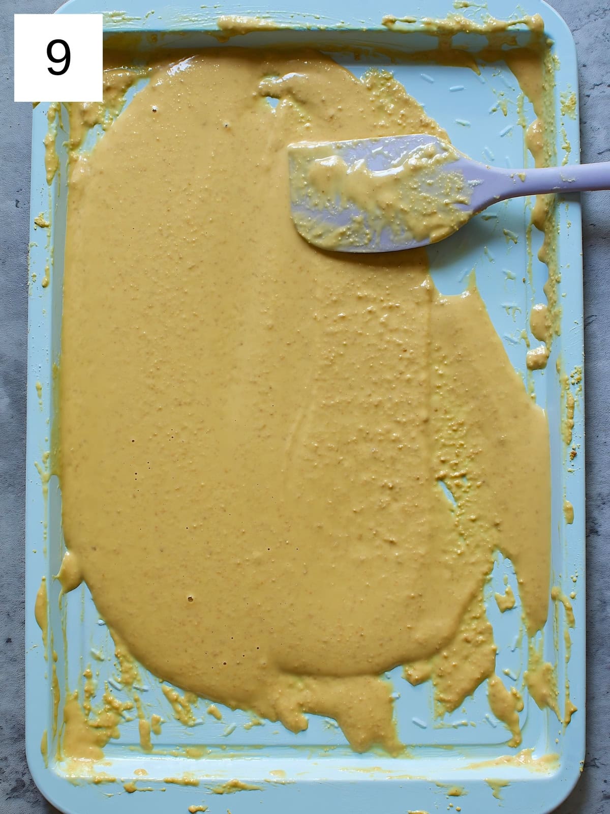 A baking spatula stirring melted white chocolate in a baking tray.