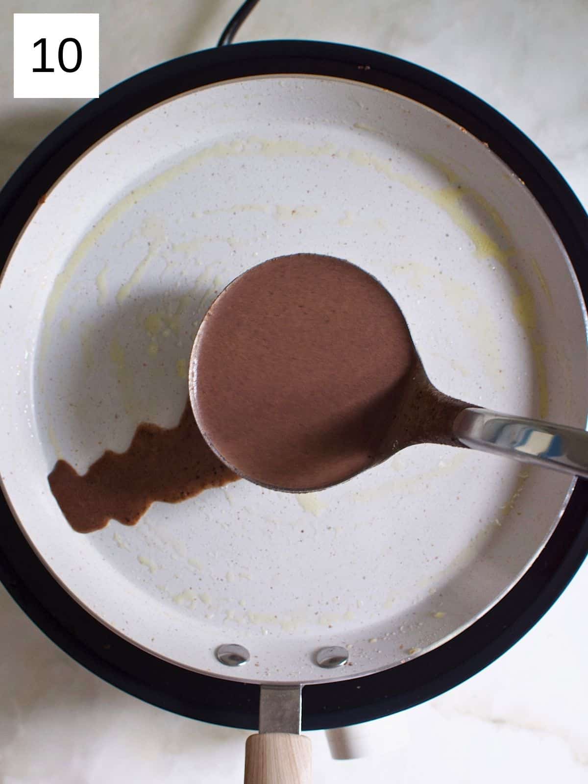 A person spreading chocolate crepe batter into the heated pan.