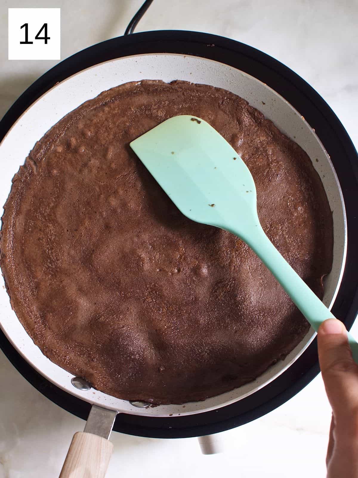 Flipped chocolate crepe in a heated pan.