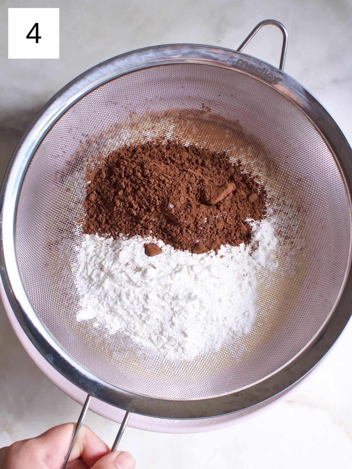 A person sifting cocoa powder and flour into a bowl of crepe batter.