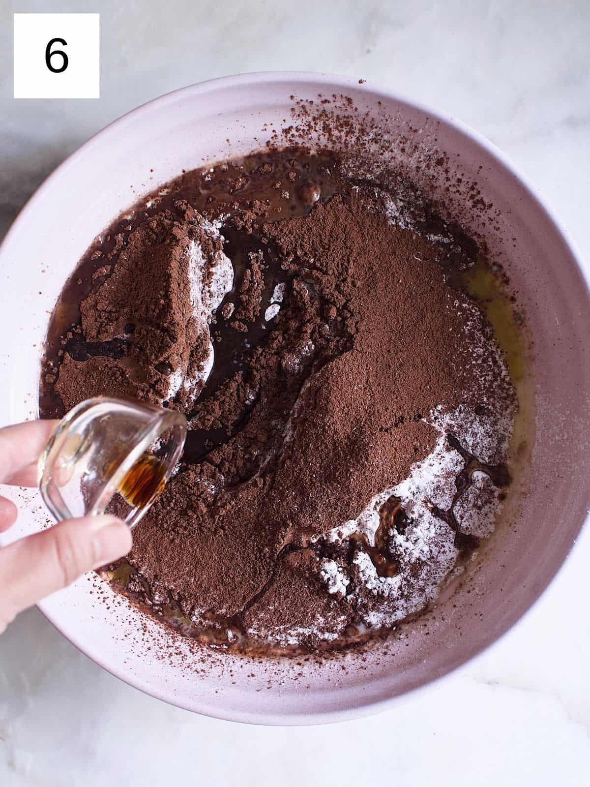 A person pouring vanilla extract into a bowl of crepe batter.