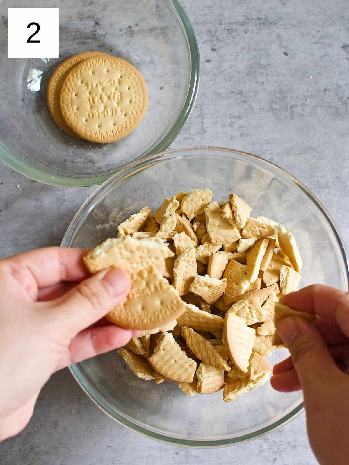 A person crushing biscuits into pieces in a bowl with their hands.