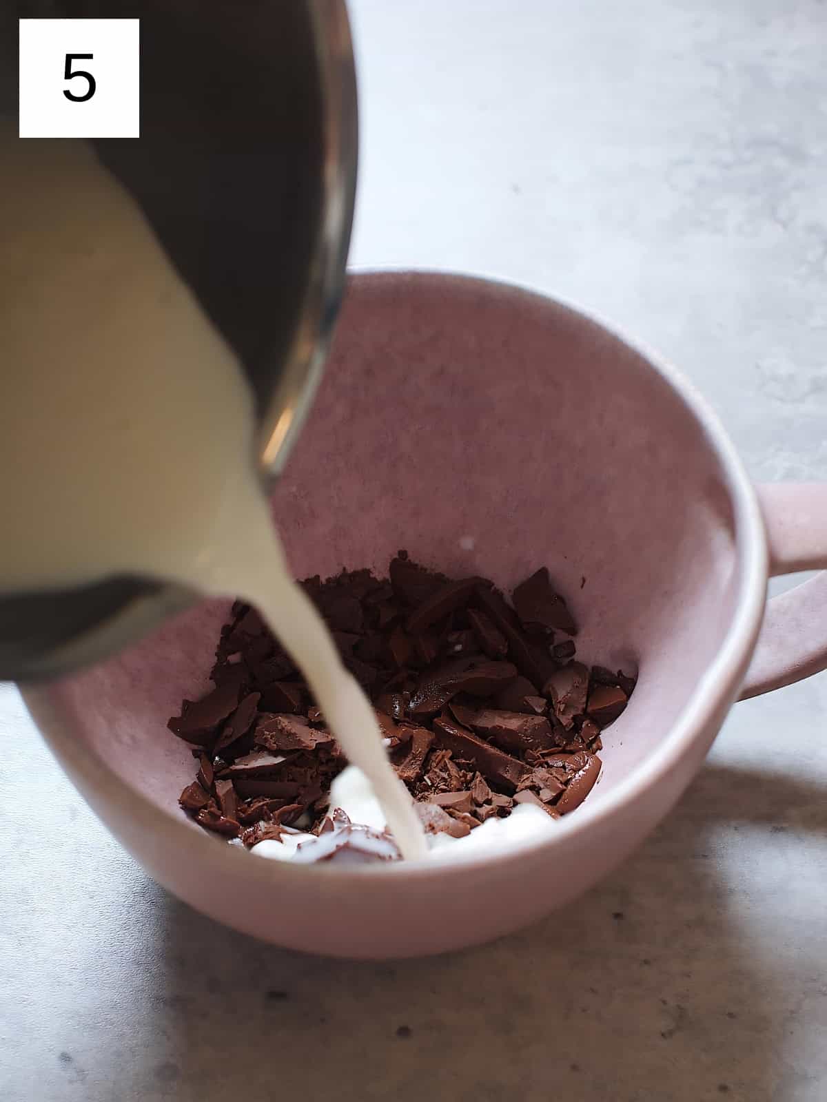 Pouring heated milk in a cup filled with minced chocolates.
