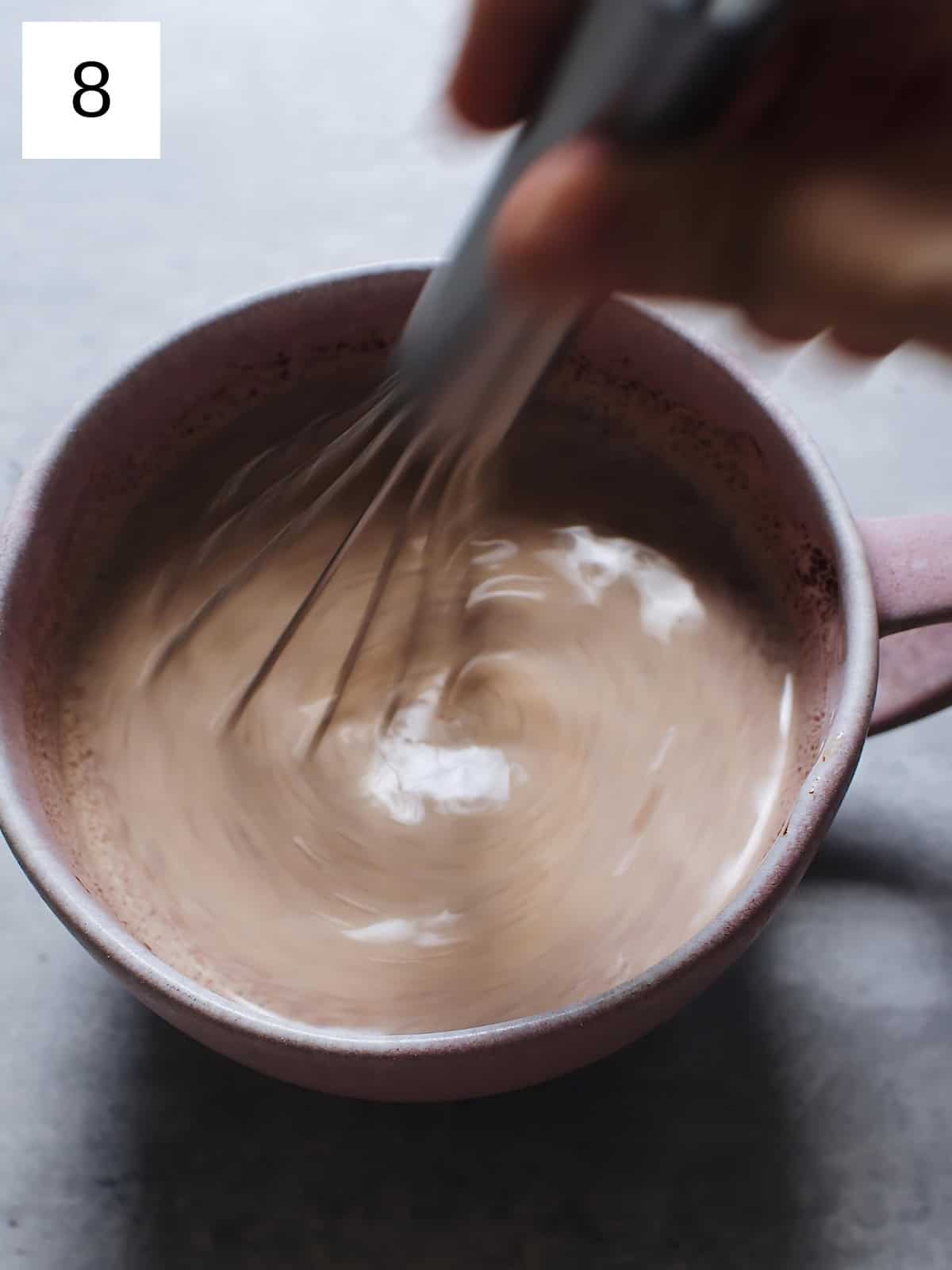 Melted chocolate mixture in a cup being mixed with a whisk.