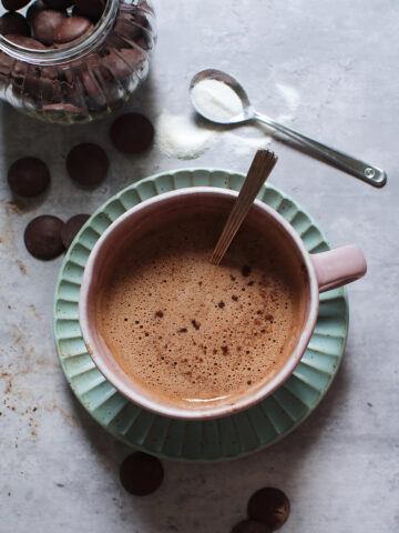 Hot chocolate collagen in a cup with a spoon next to chocolates and a spoon of collagen.