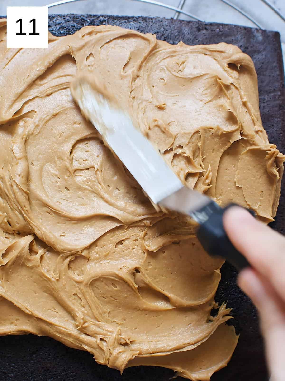 Whipped chocolate ganache being spread on a cake with a spreading knife.