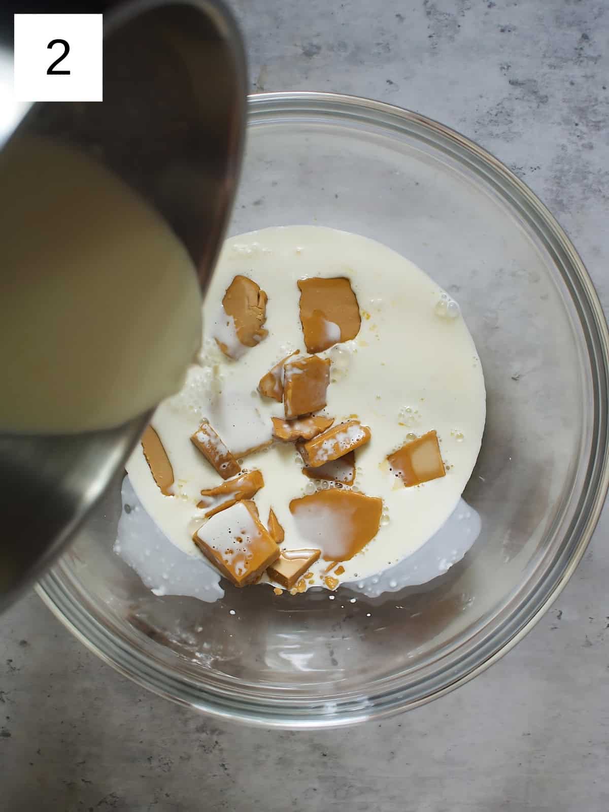 Heated heavy cream being poured on blonde chocolates in a bowl.