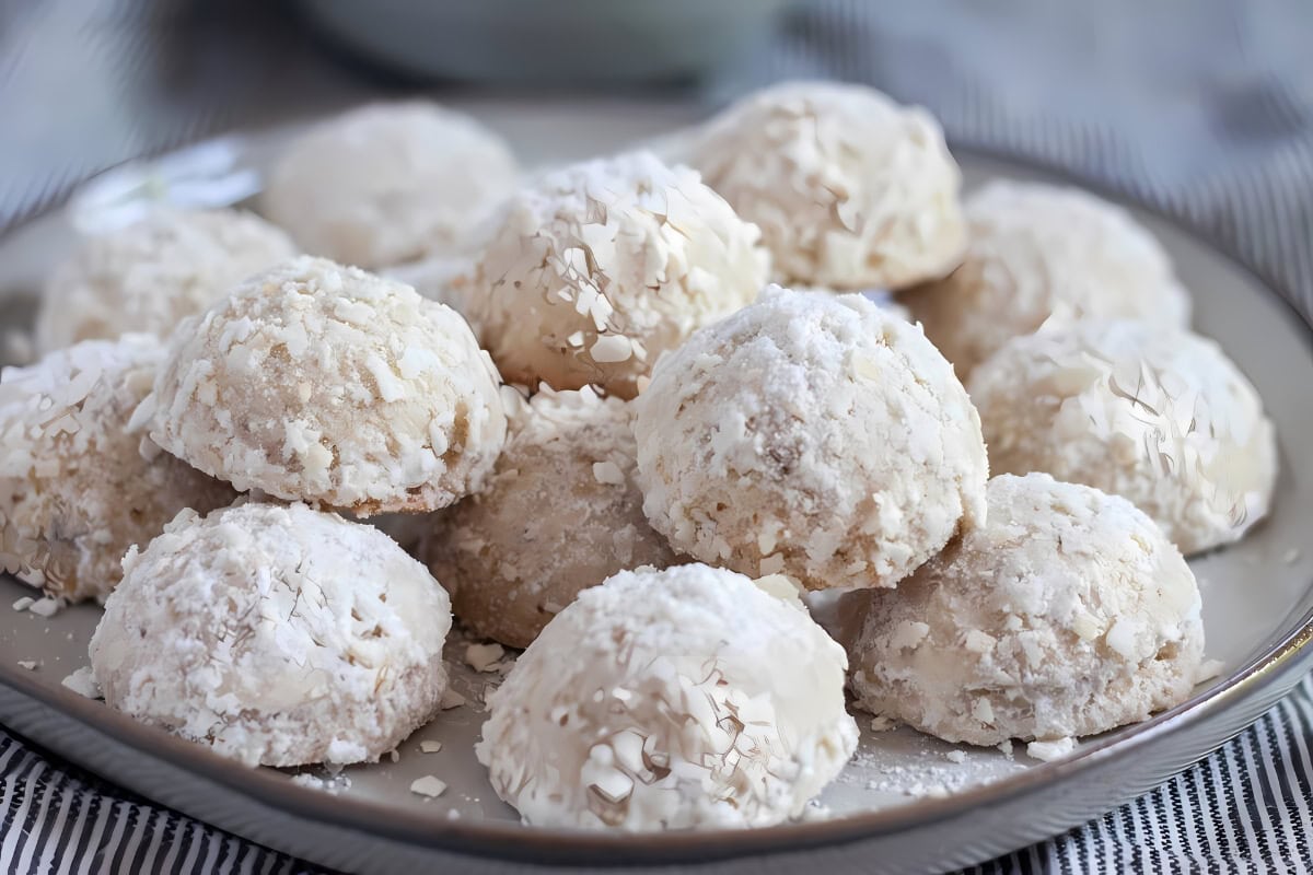 A bunch of coconut Mexican snowballs on a plate topped with coconut shavings.