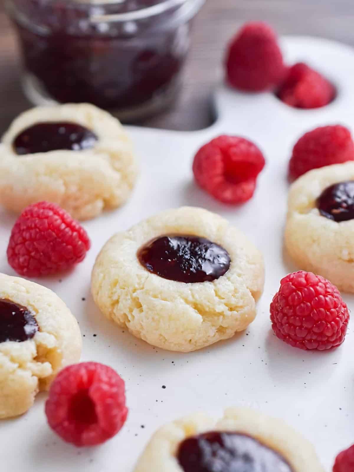 Raspberry filled cheesecake thumbprints next to raspberries.