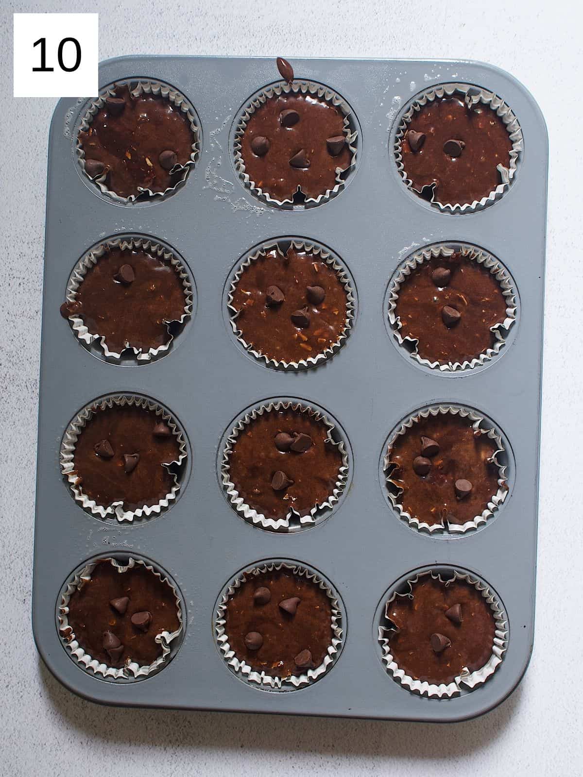 Banana chocolate protein batter topped with chocolate chips placed in a cupcake liner in a muffin tray.