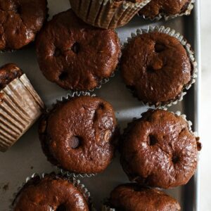 A bunch of banana chocolate protein muffins topped with chocolate chips on a tray.