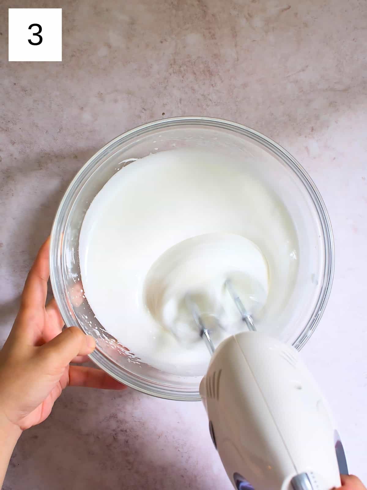 A person continuing to whisk a bowl of egg whites with a hand mixer.