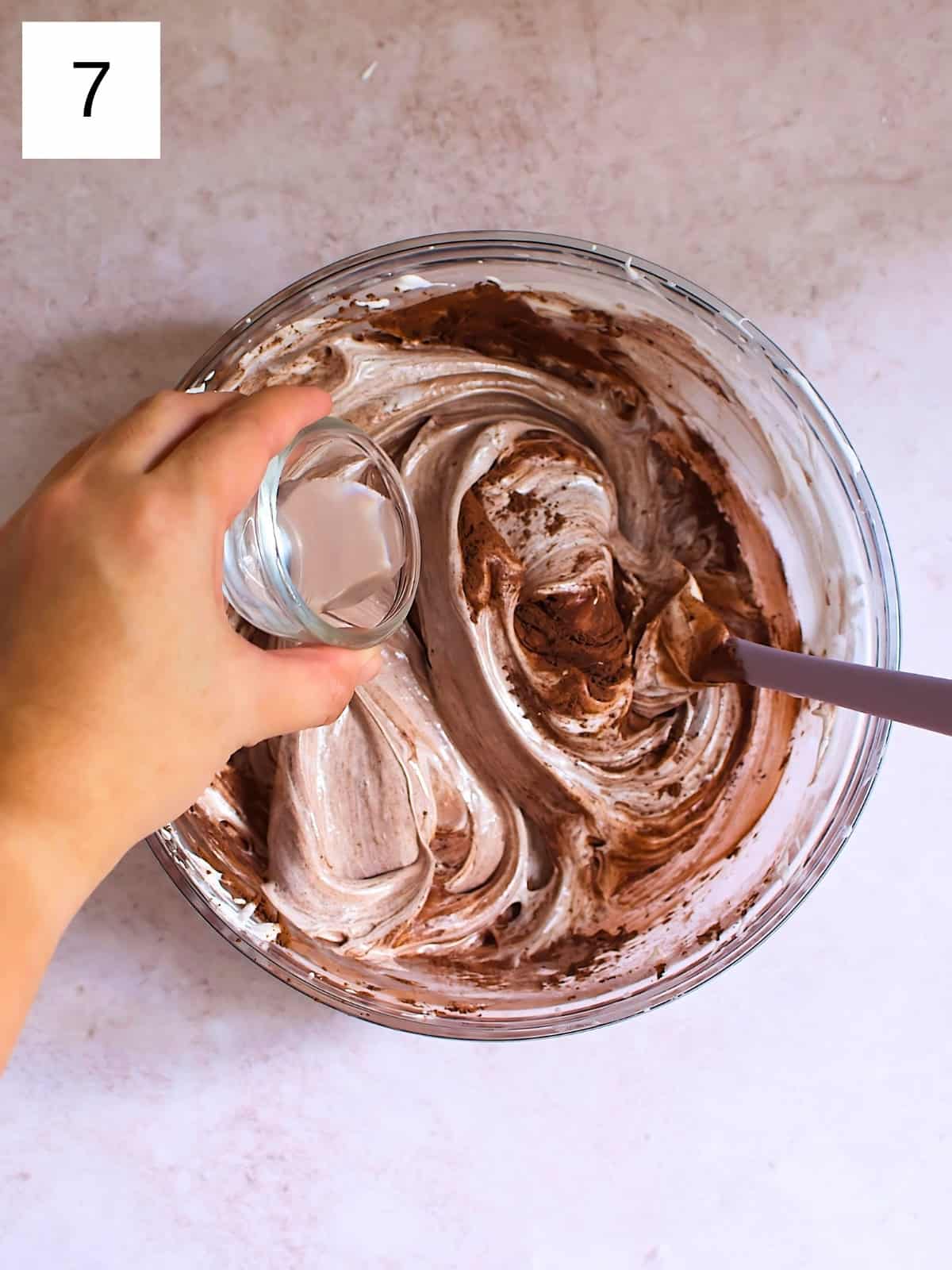 A person drizzling vinegar over a bowl of meringue with cocoa powder.