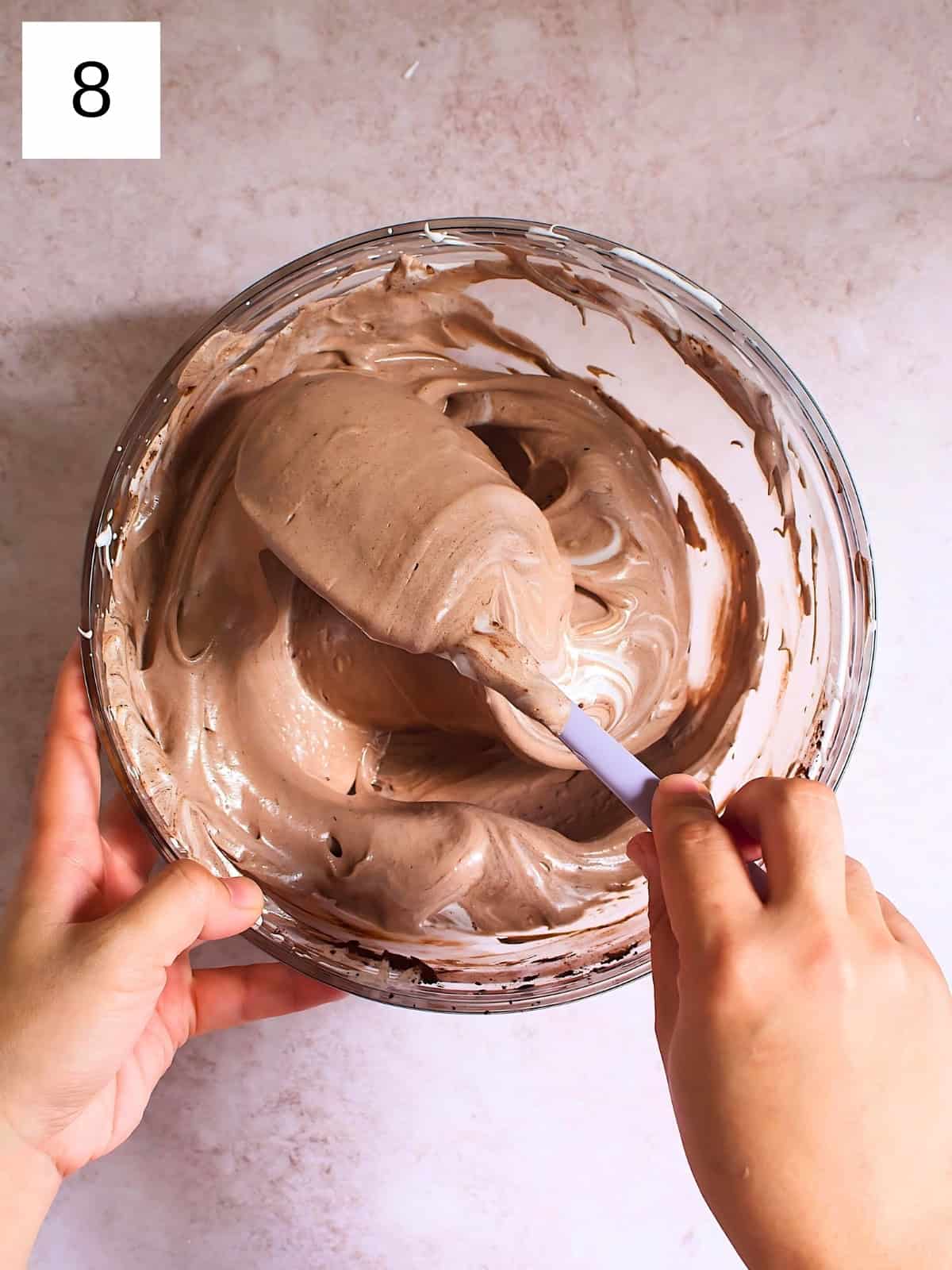 A person mixing a bowl of cocoa meringue with added white vinegar.