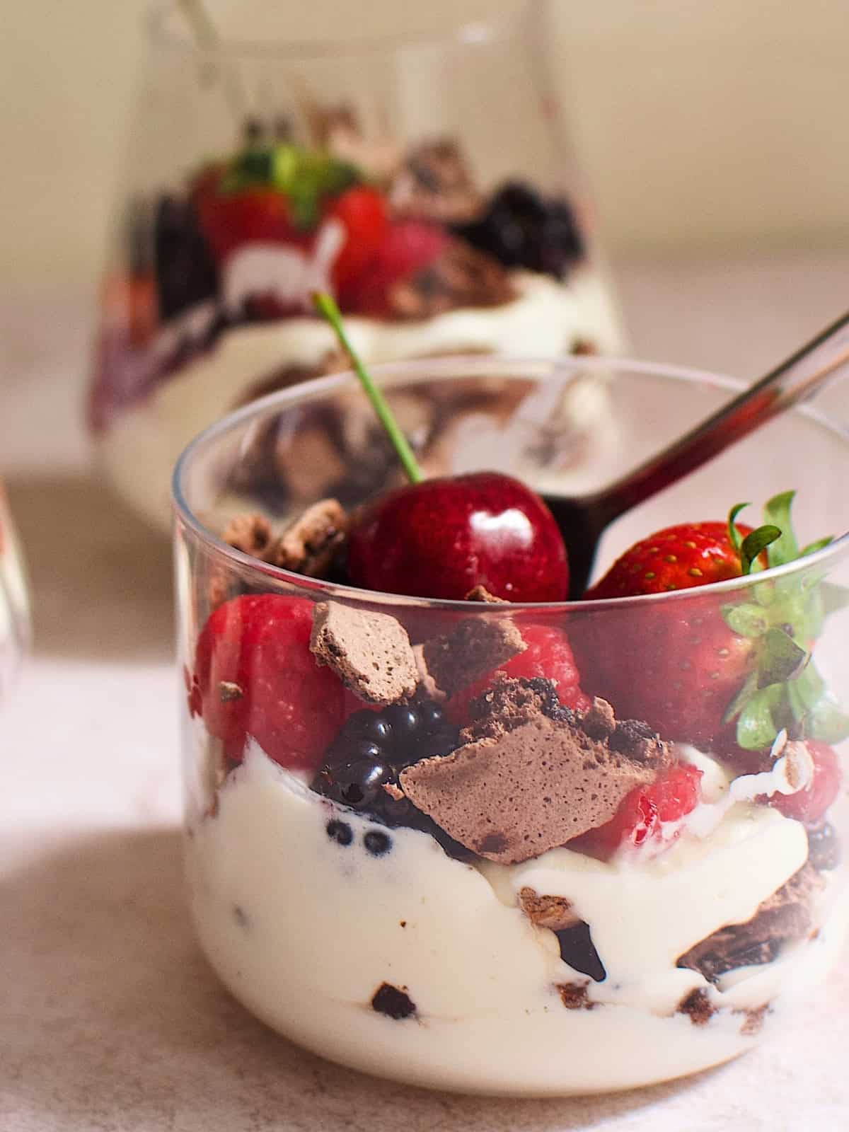 A glass of chocolate eton mess with cherries, strawberries, raspberries, and blackberries.