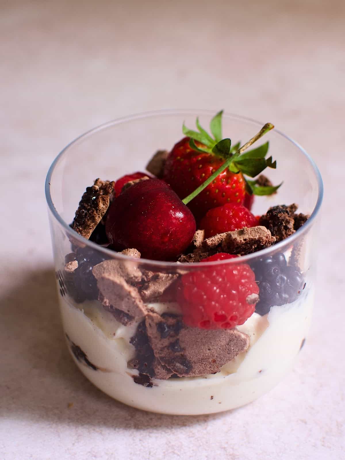 A glass of chocolate eton mess with cherries, strawberries, raspberries, and blackberries.