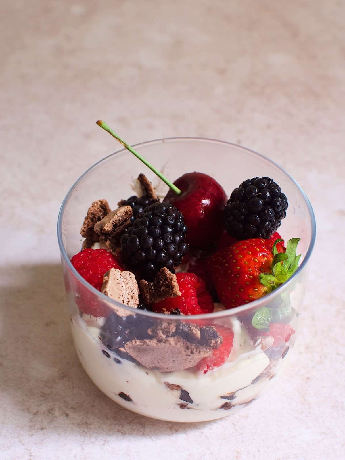 A glass of chocolate eton mess with cherries, strawberries, raspberries, and blackberries.