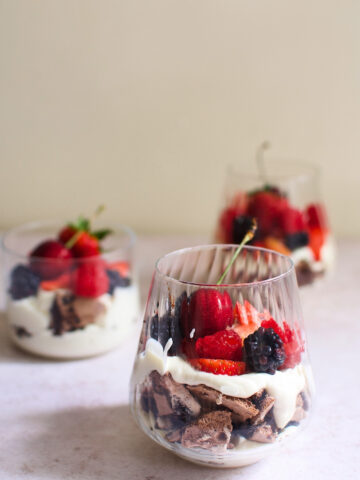 A glass of chocolate eton mess with cherries, strawberries, raspberries, and blackberries.