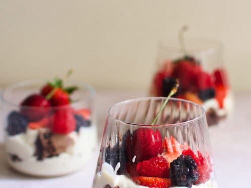 A glass of chocolate eton mess with cherries, strawberries, raspberries, and blackberries.