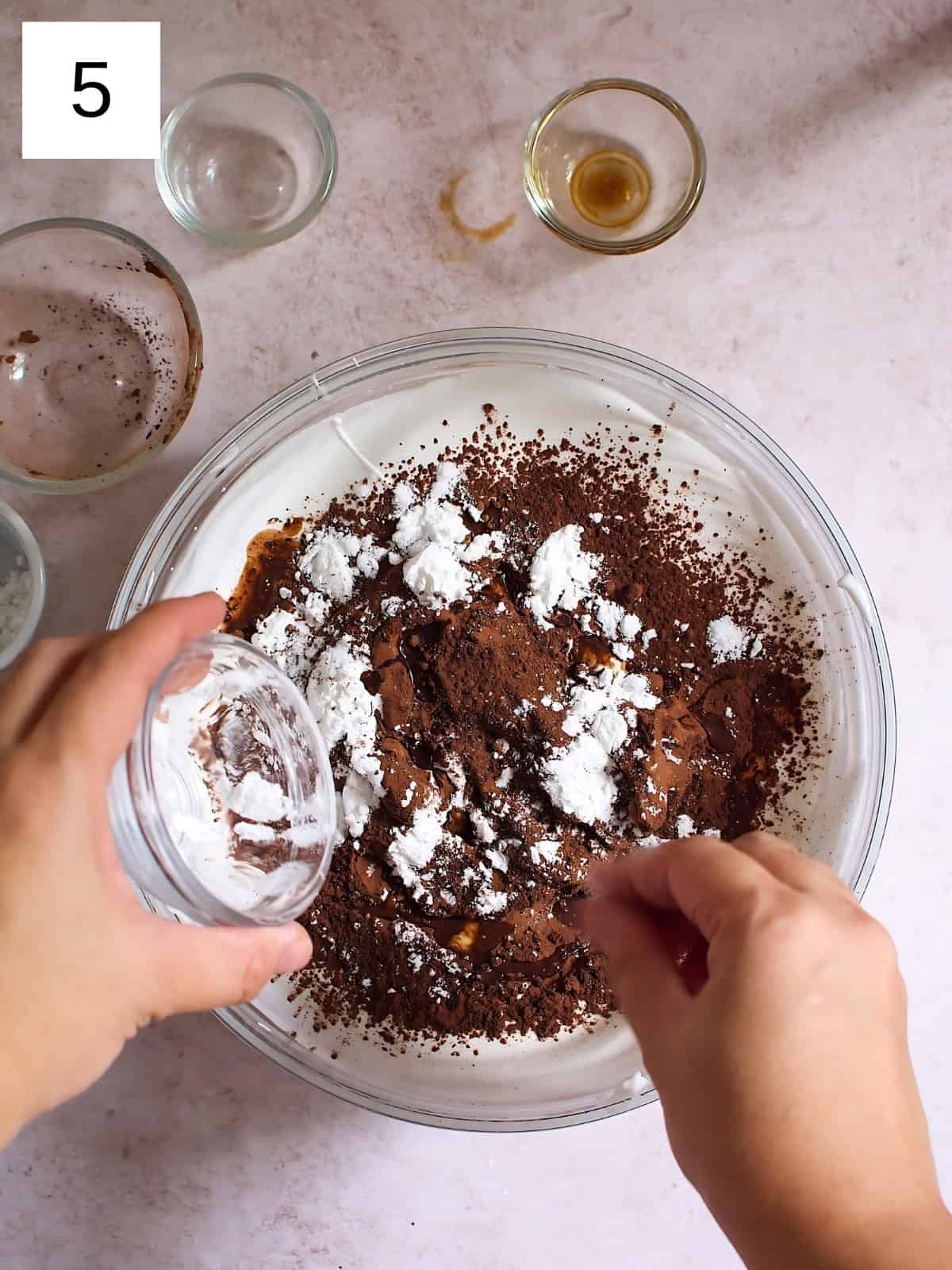 A person sprinkling a cream of tartar to a bowl of meringue mixed with cocoa powder.