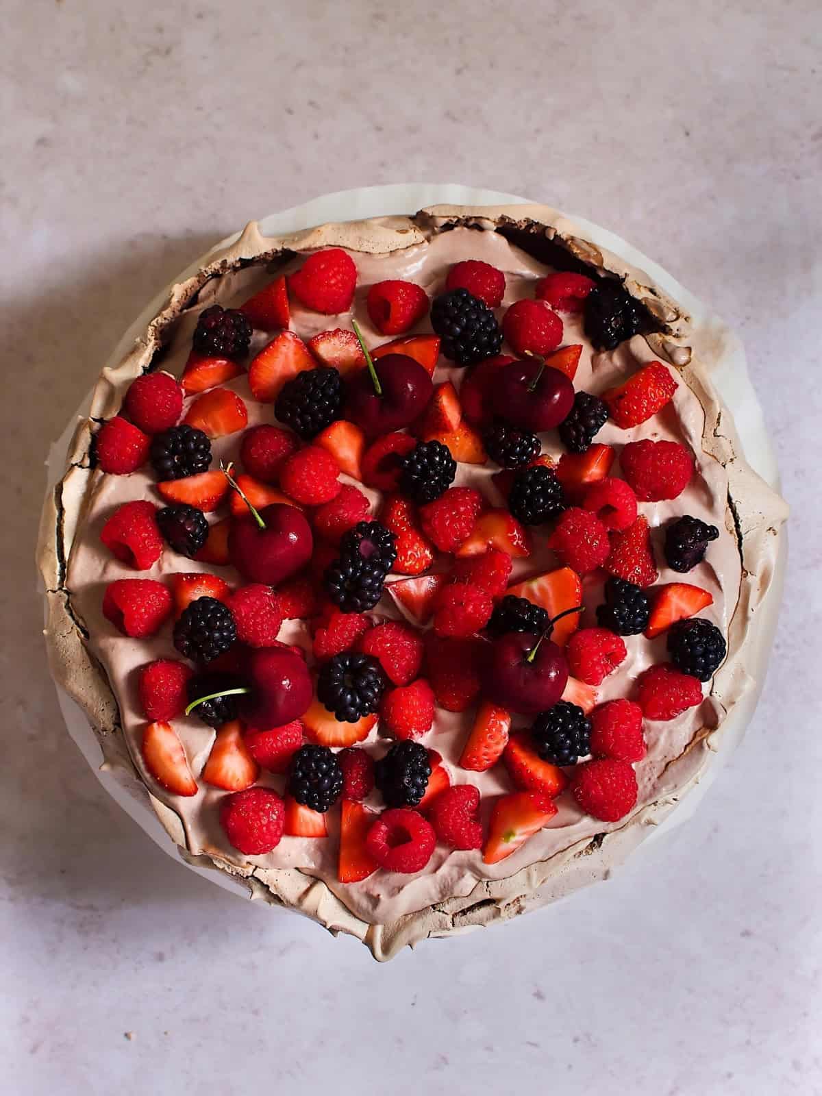 Chocolate pavlova topped with blackberry, cherry, raspberry, and strawberry.