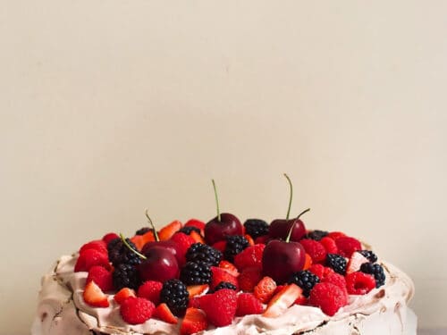 Chocolate pavlova topped with blackberry, cherry, raspberry, and strawberry.