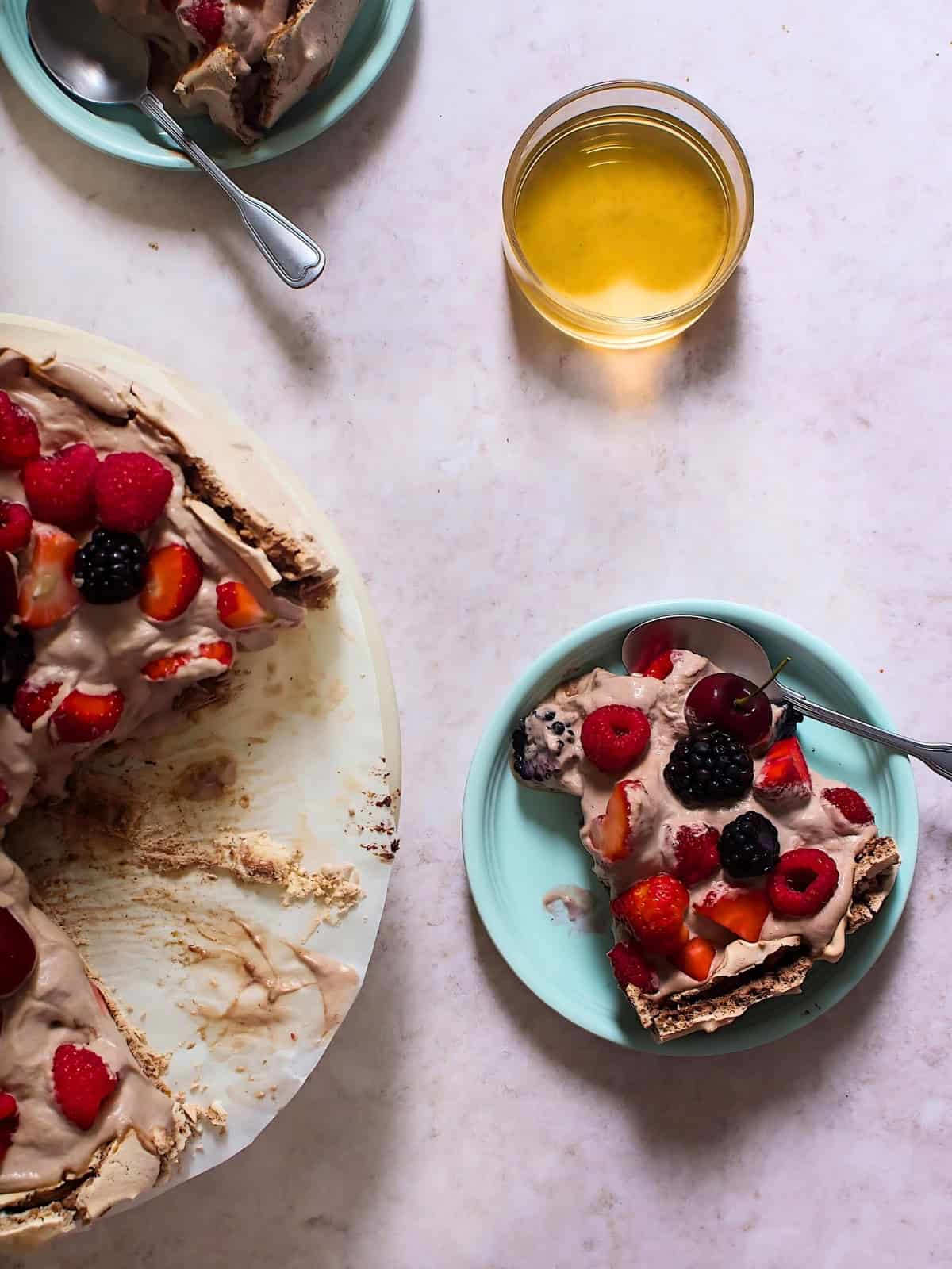 A slice of chocolate pavlova in a plate topped with different kinds of berries.