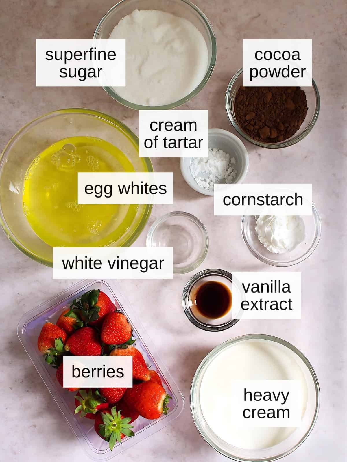 Chocolate pavlova recipe ingredients including superfine sugar, cocoa powder, cream of tartar, egg whites, cornstarch, white vinegar, vanilla extract, strawberries, and heavy cream.