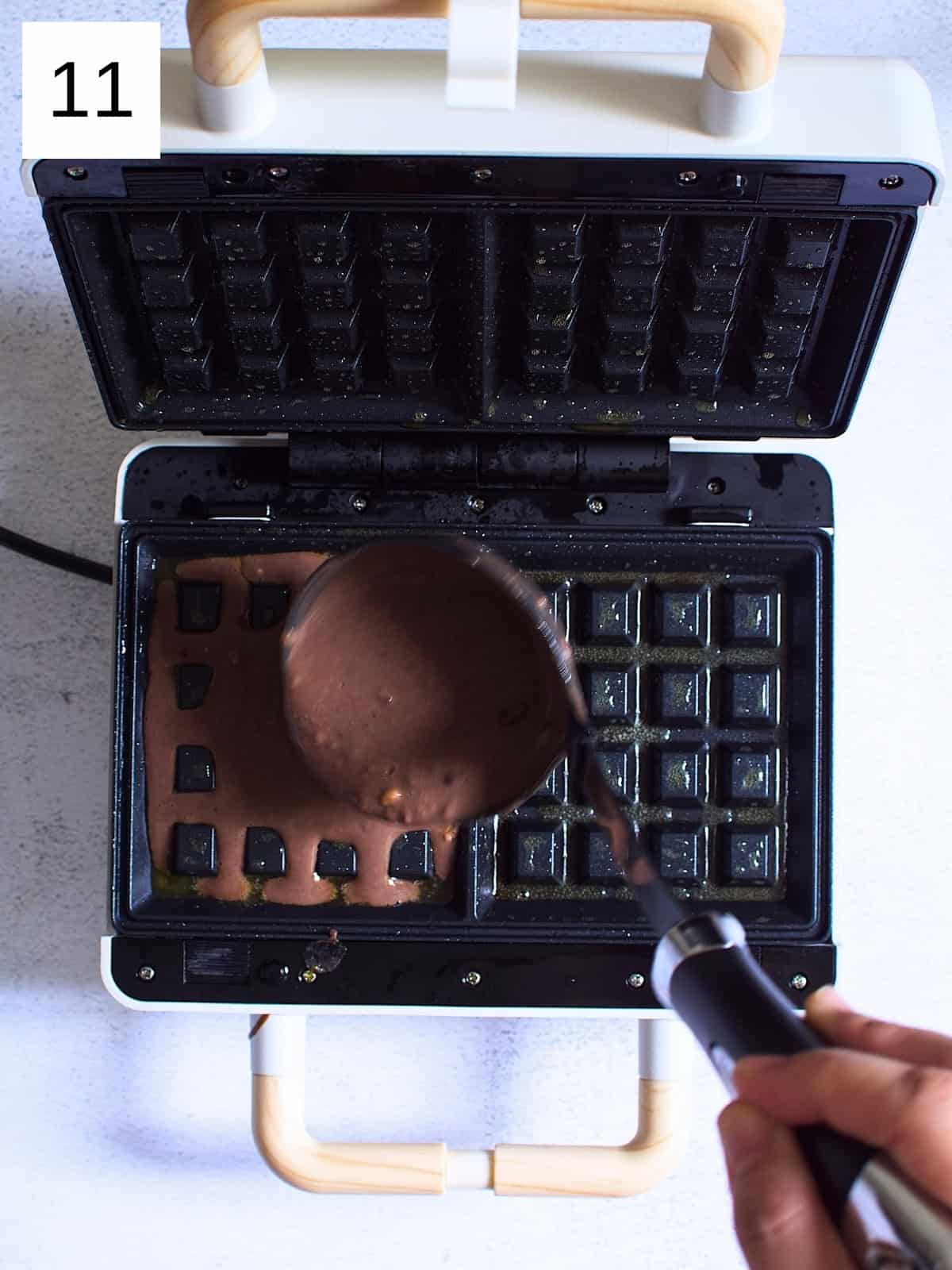 Chocolate waffle batter being poured in a waffle maker.