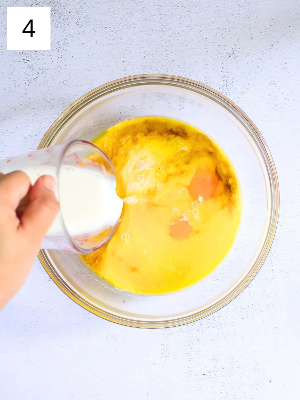 Milk being poured in a bowl of eggs, melted butter, and vanilla extract