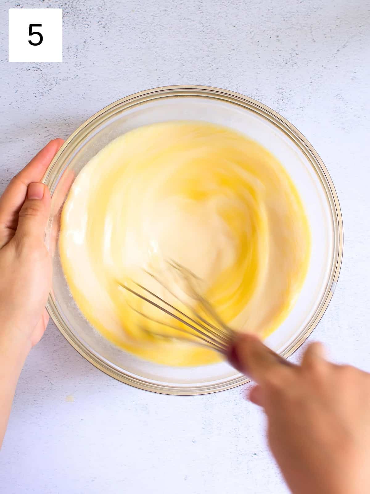 A bowl of milk, eggs, melted butter, and vanilla extract being whisked.