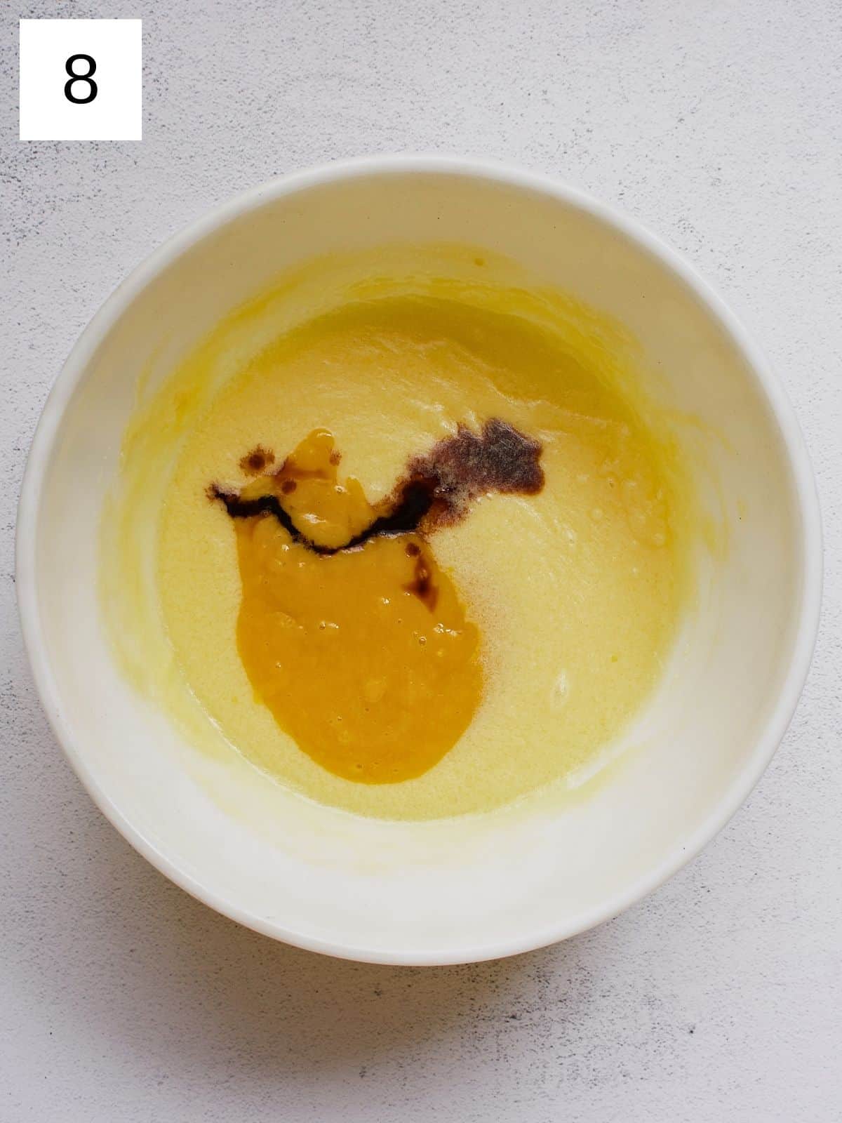 A bowl of whisked melted butter, sugar, and egg with added mango puree and vanilla extract.