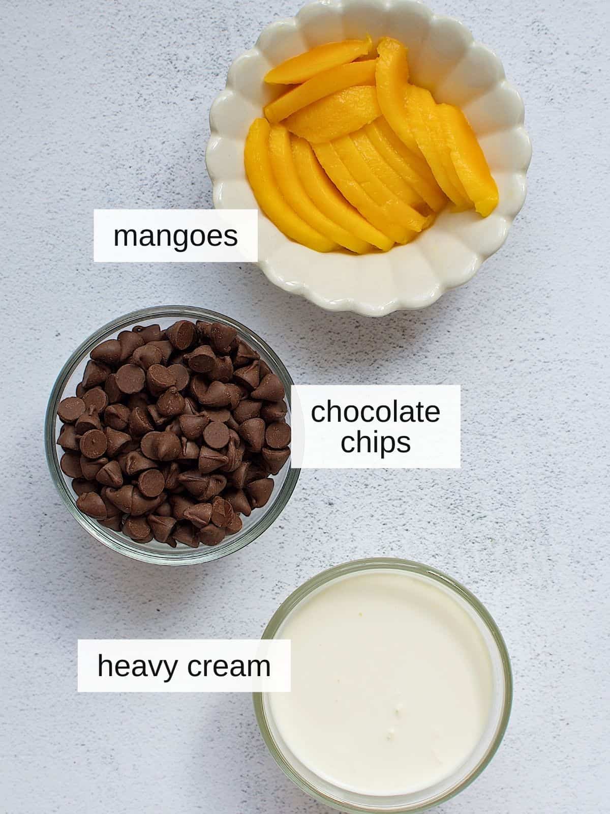 Chocolate ganache and mango topping ingredients with mangoes, chocolate chips, and heavy cream.