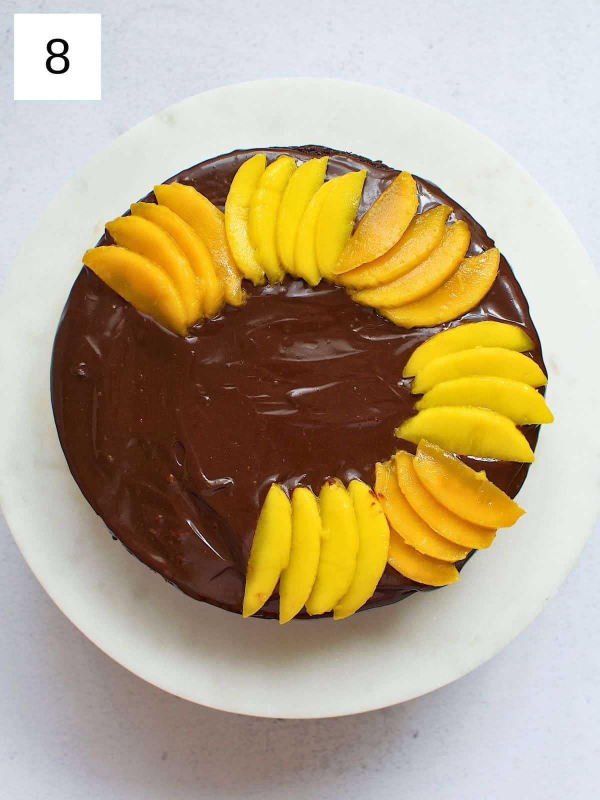 Slices of mangoes being arranged on top of a chocolate cake.