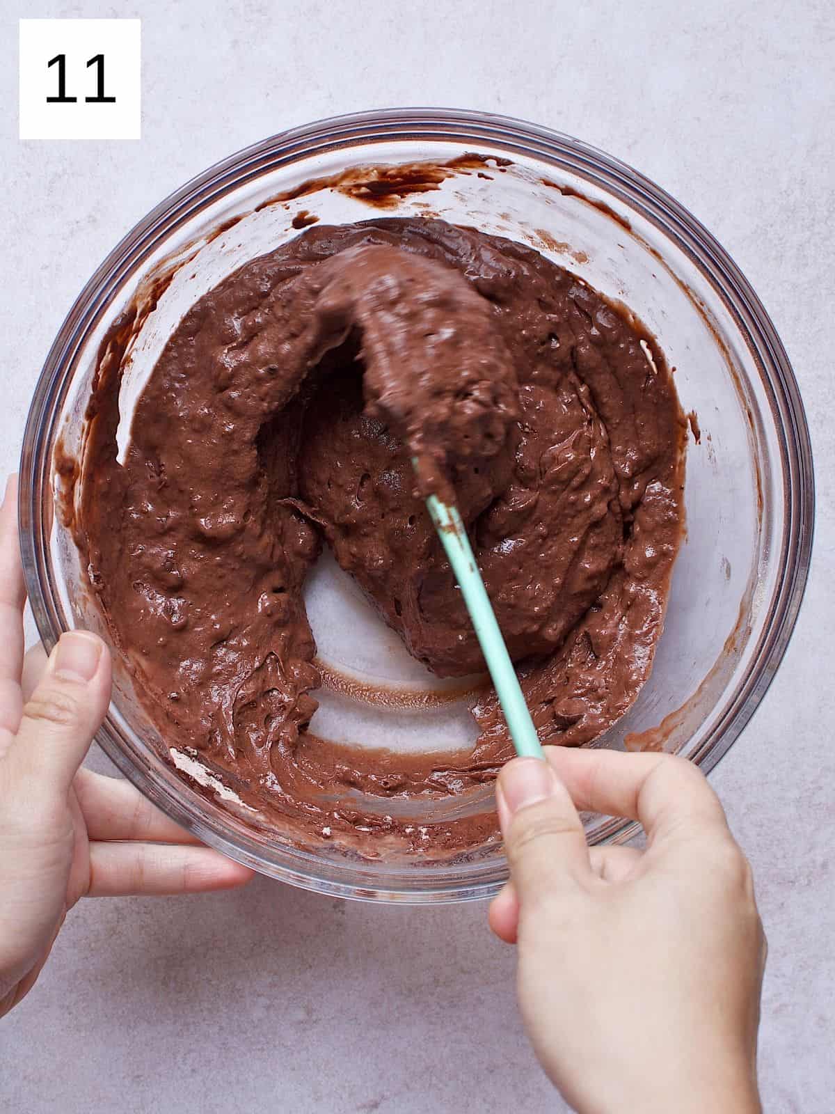 A person folding chocolate pancake batter with chocolate chips.