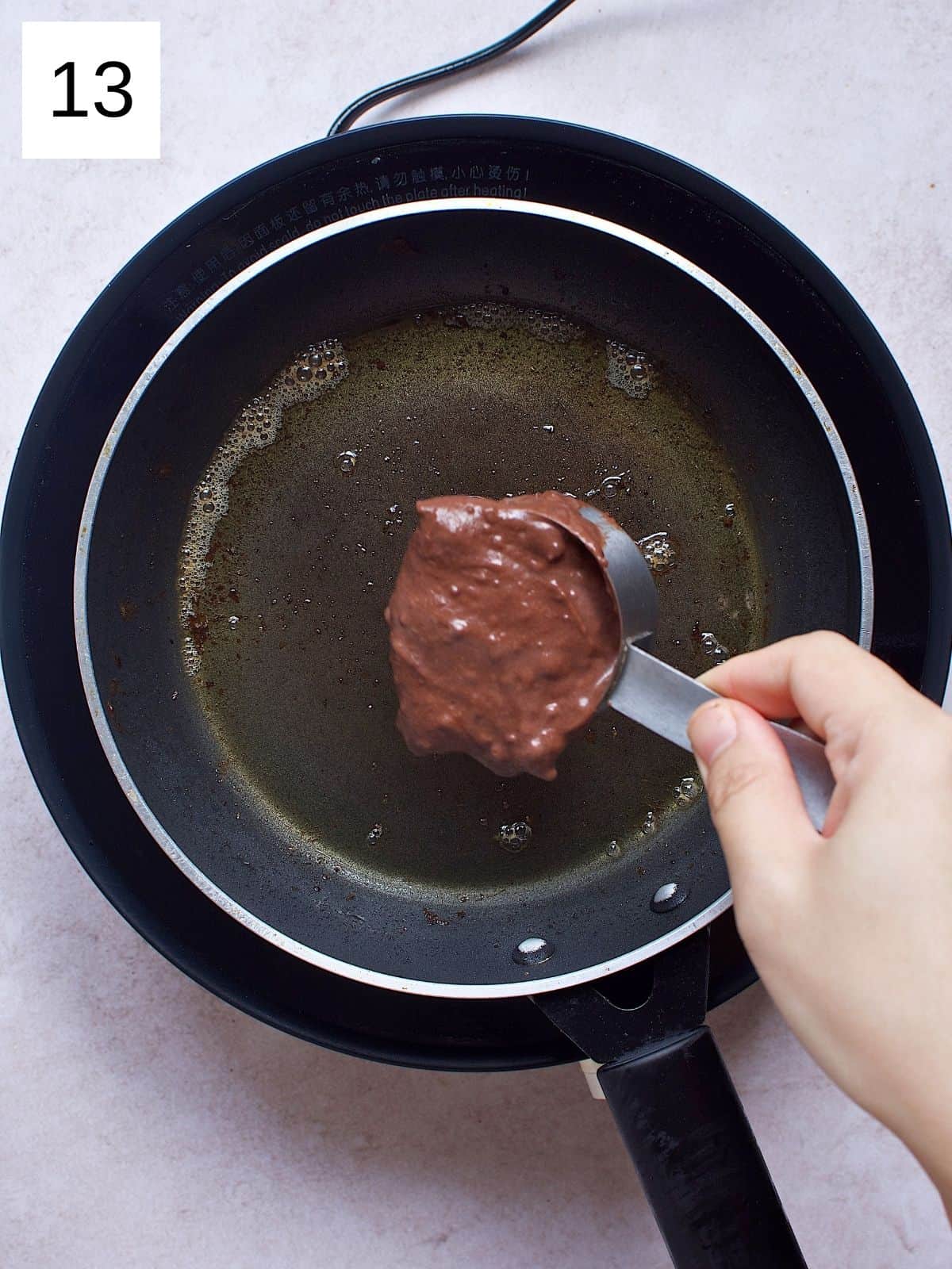 A scoop of chocolate pancake batter ready to be placed in a skillet.