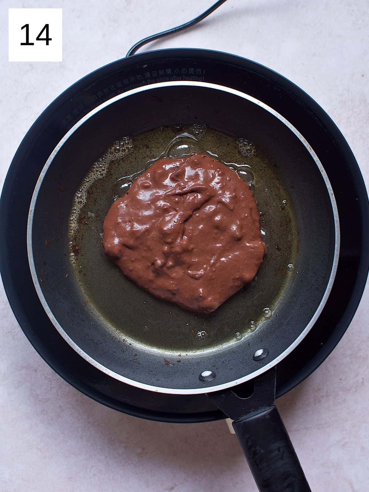 Chocolate pancake batter being cooked in a heated skillet.