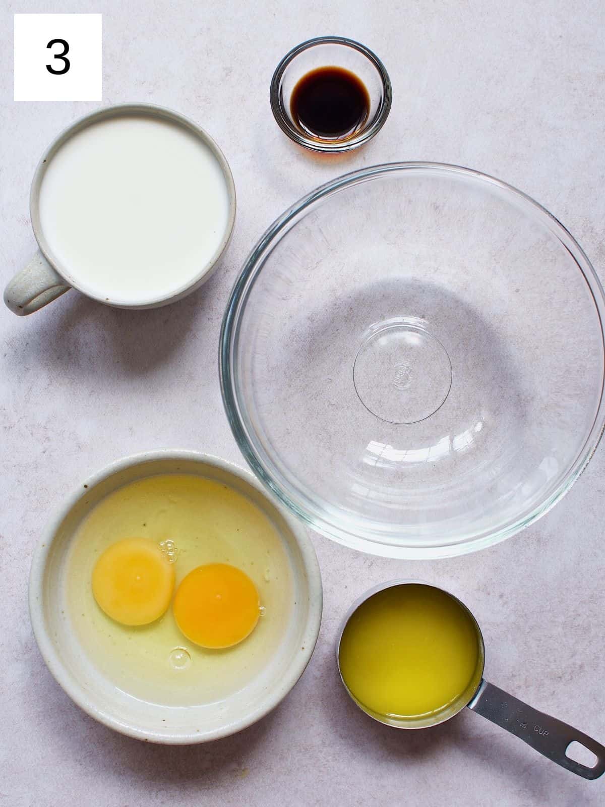 Milk, egg, melted butter, and vanilla extract beside a bowl.