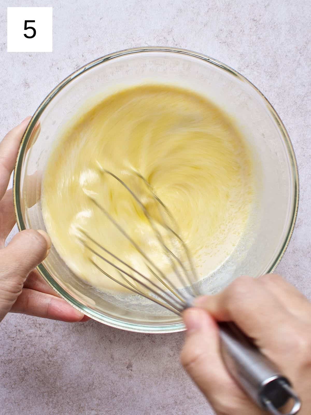 A person whisking milk, egg, melted butter, and vanilla extract in a bowl.