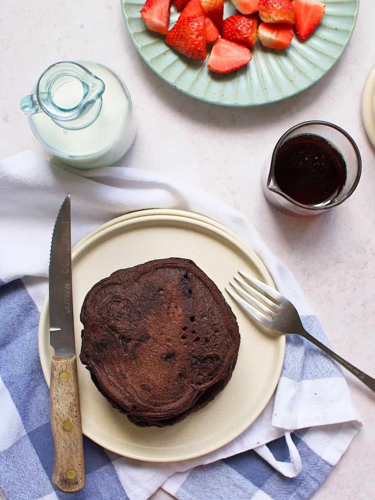 Chocolate pancaked on a plate next to a jar of maple syrup.