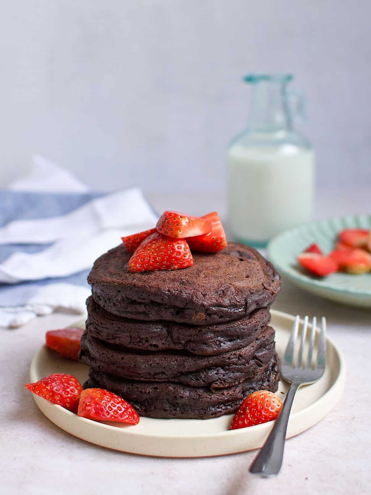 Stacked chocolate pancakes with strawberries on a plate.