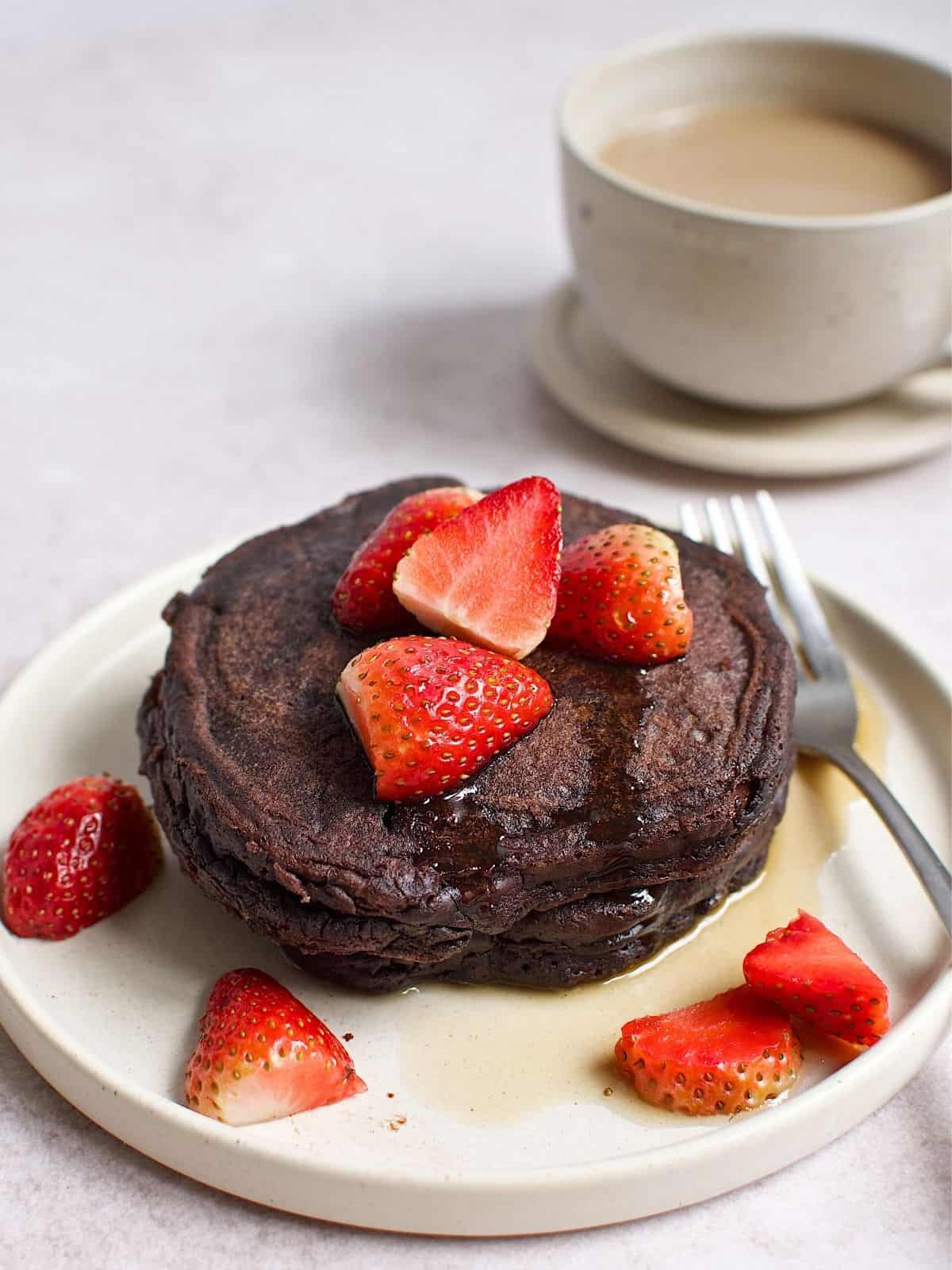 Stacked chocolate pancakes on plate, topped with strawberries.