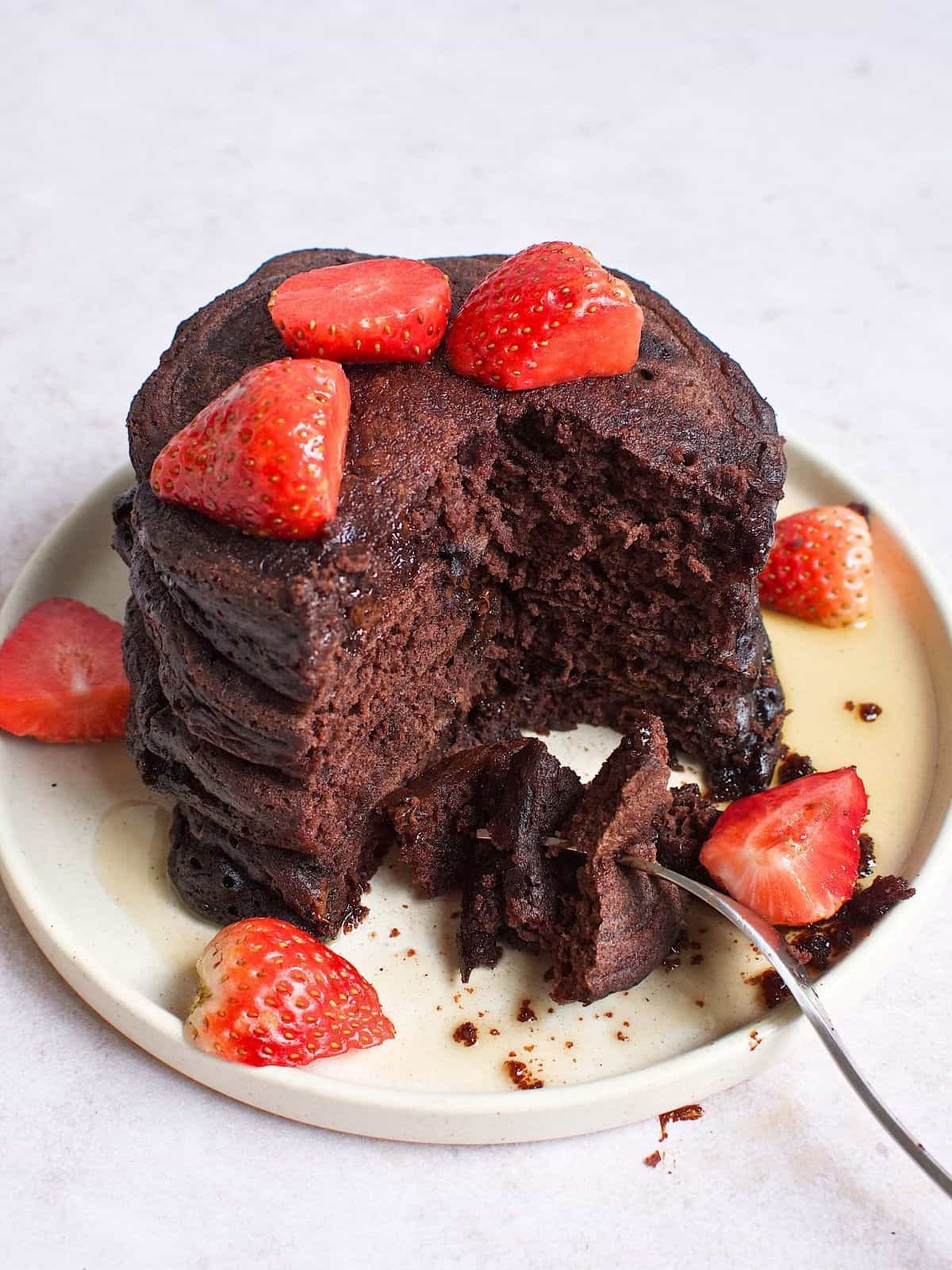 Stacked chocolate pancakes with strawberries on a plate.