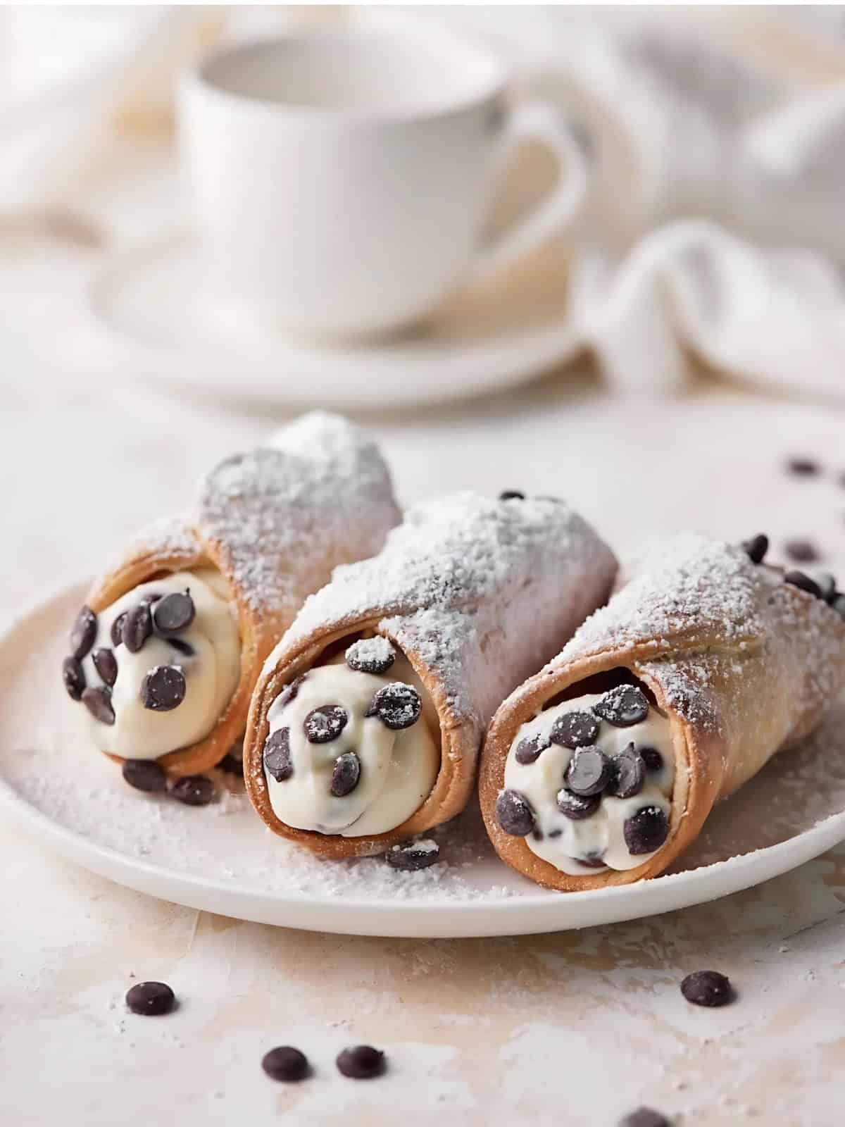 A plate of cannoli with chocolate chips covered with powdered sugar.