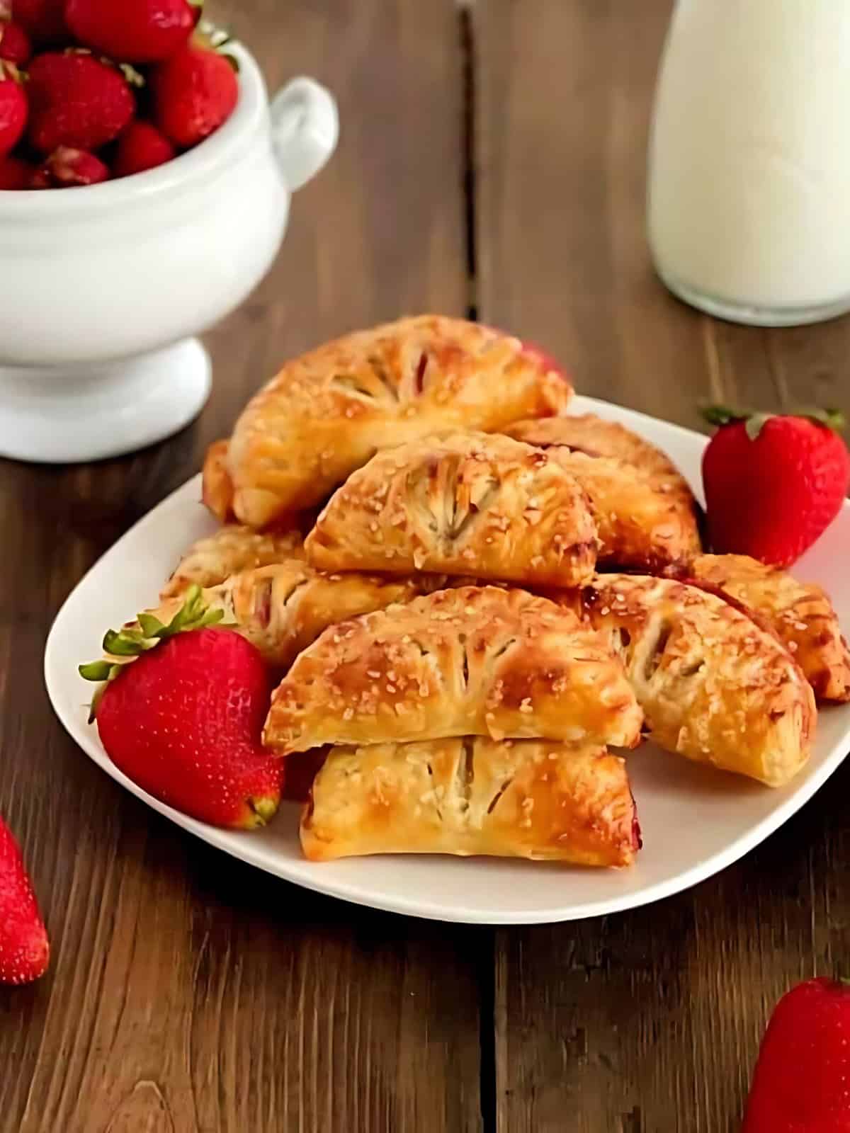 A plate full of strawberry turnovers next to strawberries.