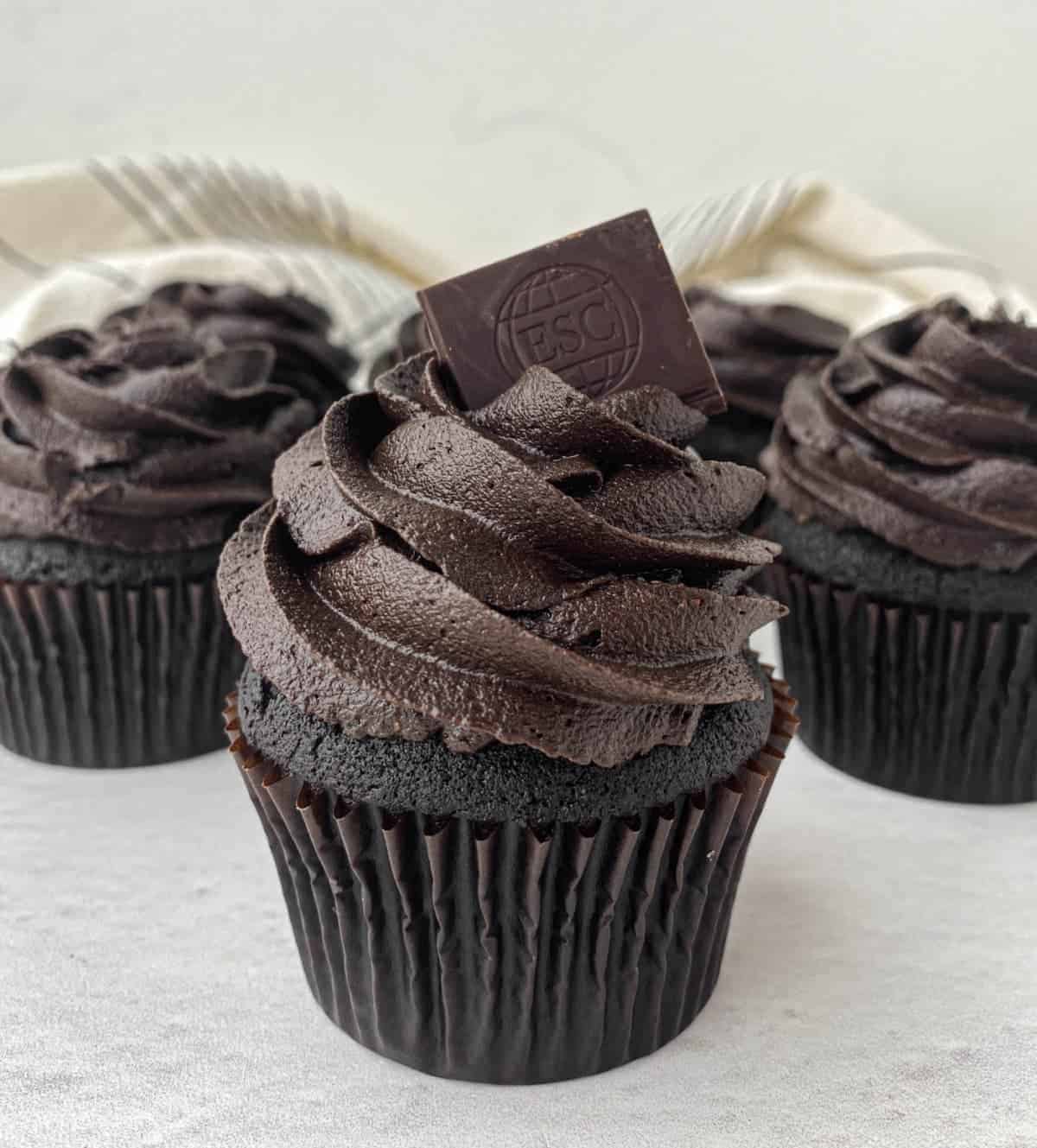 Black chocolate cupcakes topped with chocolate frosting and a piece of chocolate.