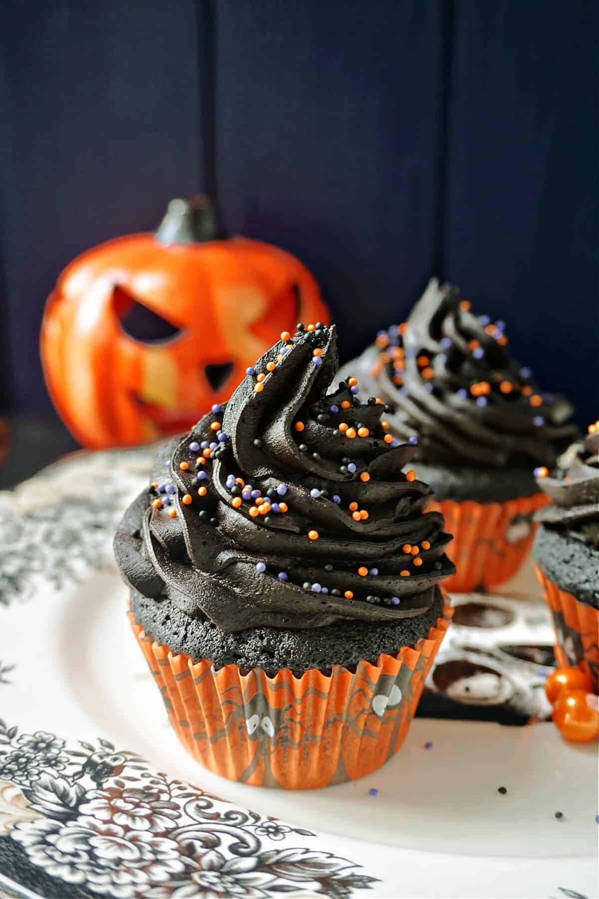 Jack-o-lantern themed black cupcakes with chocolate frosting topped with sprinkles.