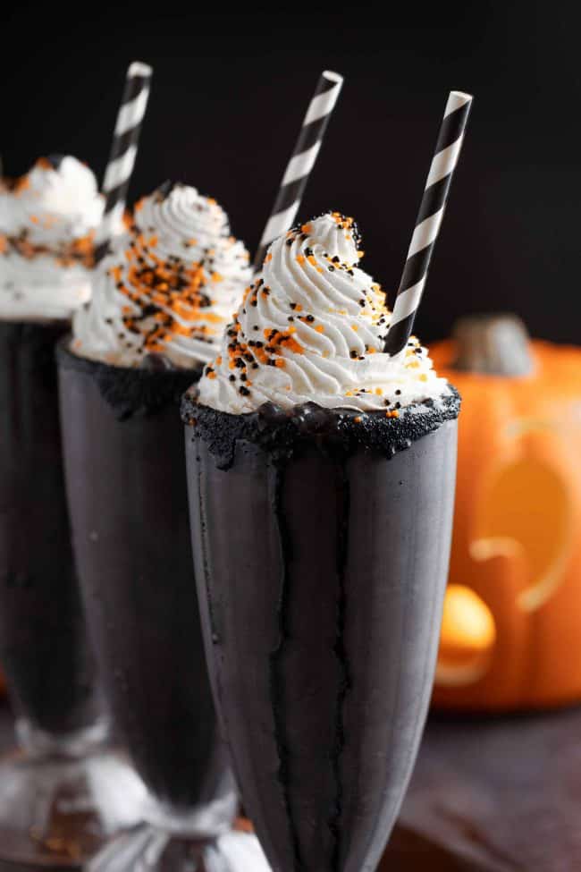 Halloween themed black milkshake topped with frostings, sprinkles, and stick biscuits.