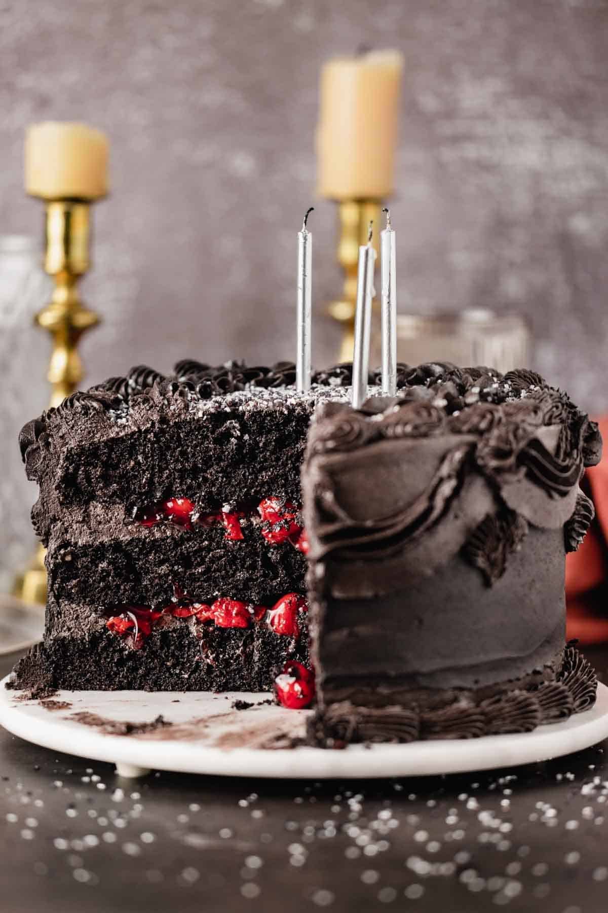 Black velvet cake with cherry filling topped with candles and frosting.